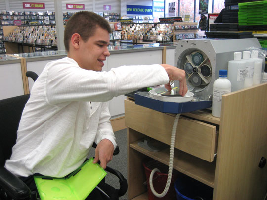 Youth who is a wheelchair user puts a CD in a machine to be cleaned
